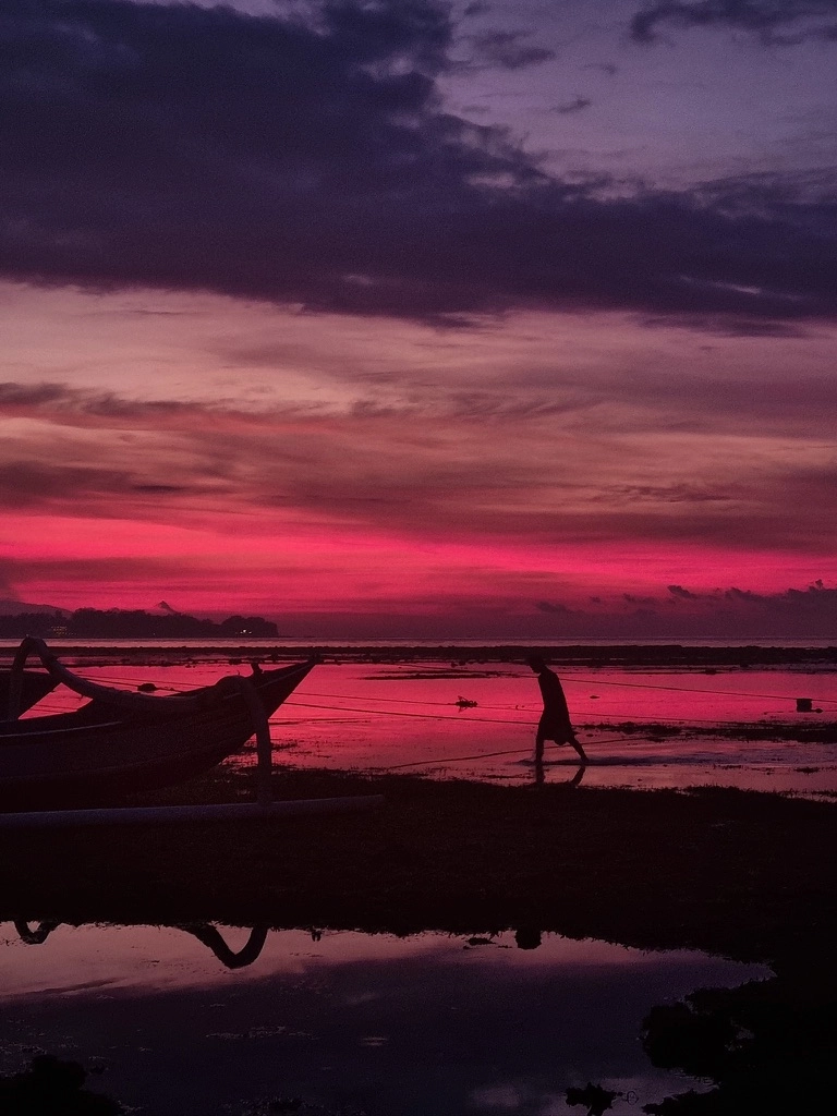 Coucher de soleil rose fuschia, avec une silhouette de pêcheur marchant sur le sable