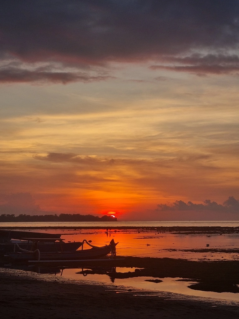 Un coucher de soleil époustouflant sur les iles gili, lueur orangée et silhouette de pêcheurs et de bateau 