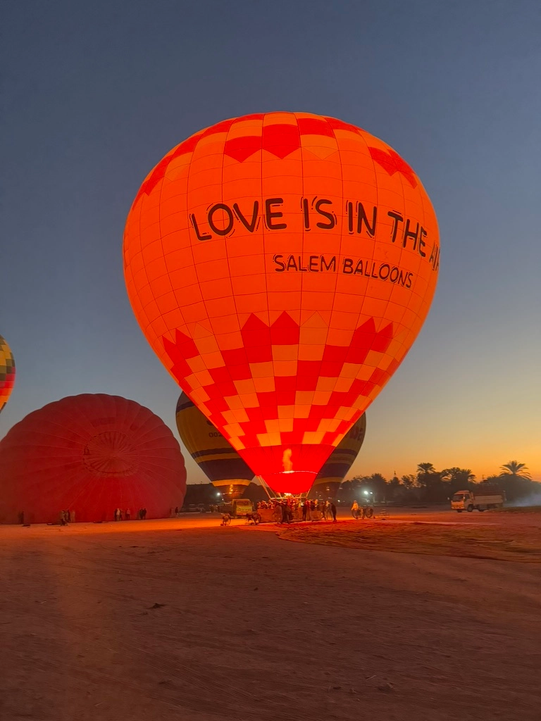Décollage d'une montgolfière rouge, écriture Love is in the air au milieu du désert