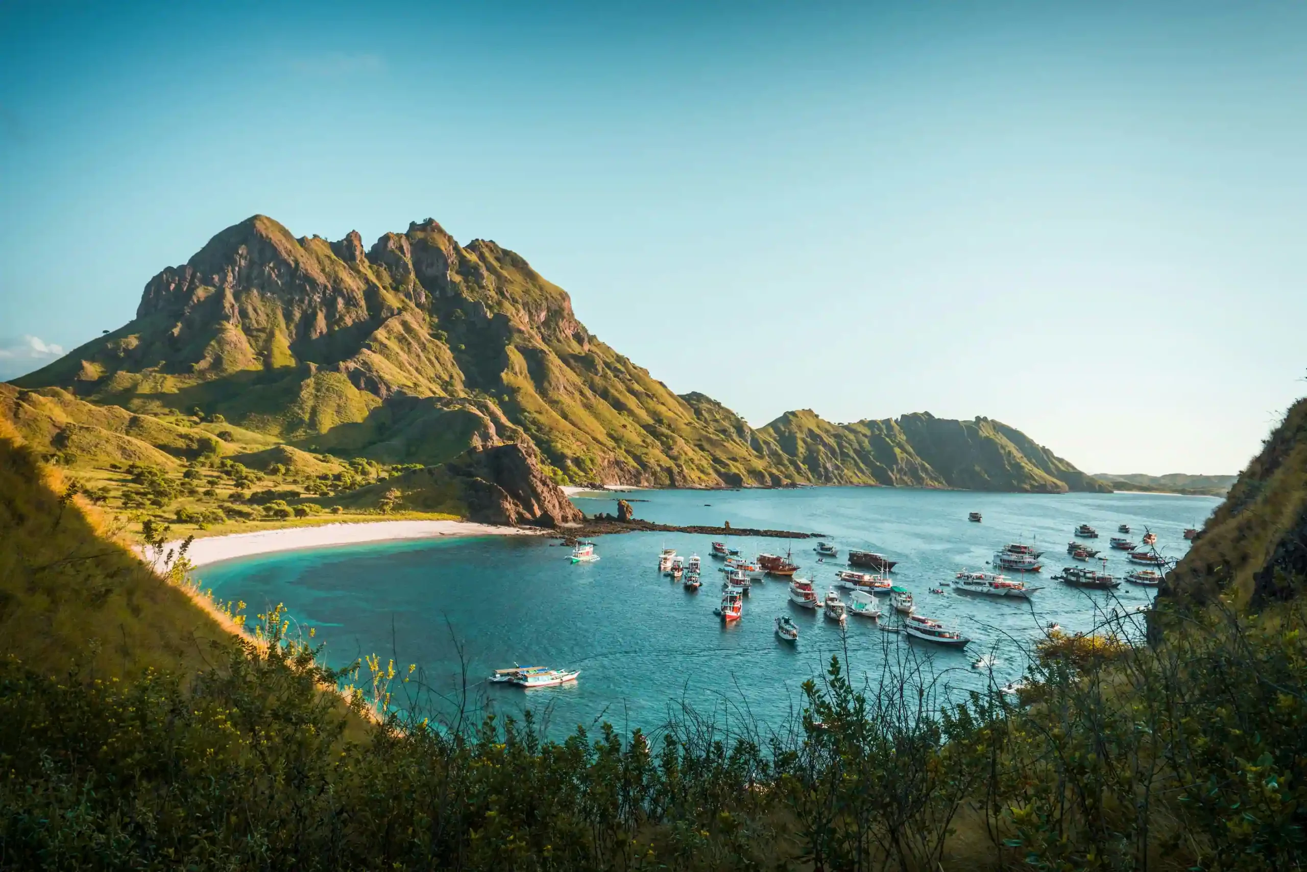 L'ile de Padar dans les Komodo en Indonésie. Une baie d'un bleu échantant devant une plage de sable blanc et quelques bateaux à la mer