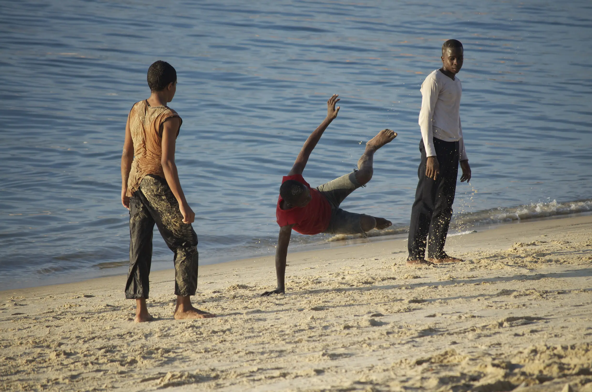 Des jeunes qui dansent la capoeira sur la plage